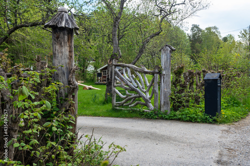 Beautiful authentic wooden fence with entrance gate around the village house. Metal black mailbox near the road. Landscape garden design with trimmed green lawn.