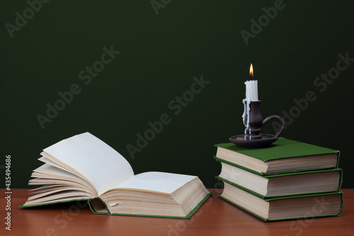 open blank book and stack of books with burning candles on green background