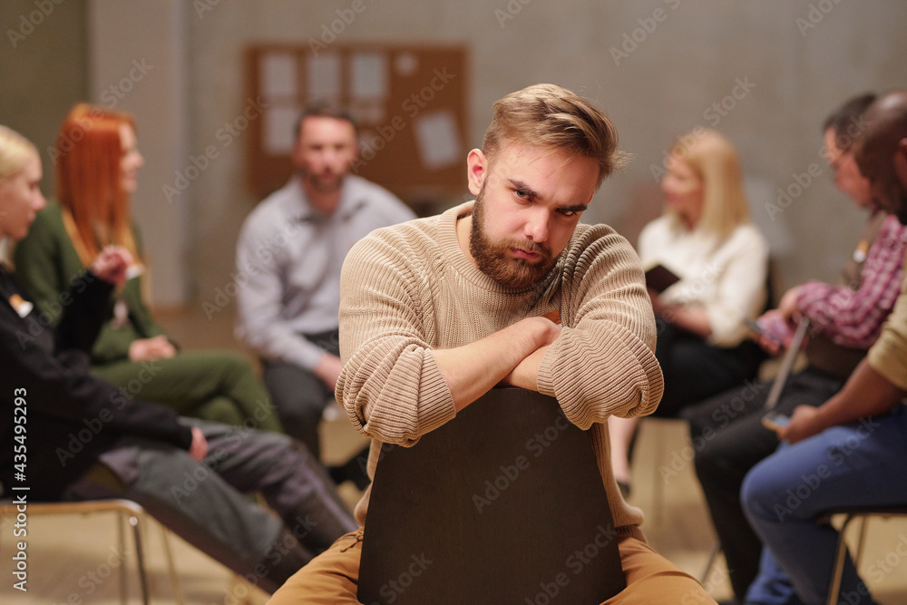 Fototapeta premium Frowning guy with beard sitting on chair during psychological session