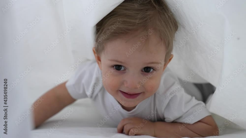Happy kid crawling under the covers. Happy family. Kid crawling on bed under white covers. Kid on bed crawling under white covers. Happy smiling kid plays. Child crawls under covers to his mother Happy kid crawling under the covers. Happy family. Kid crawling on bed under white covers. Kid on bed crawling under white covers. Happy smiling kid plays. Child crawls under covers to his mother
