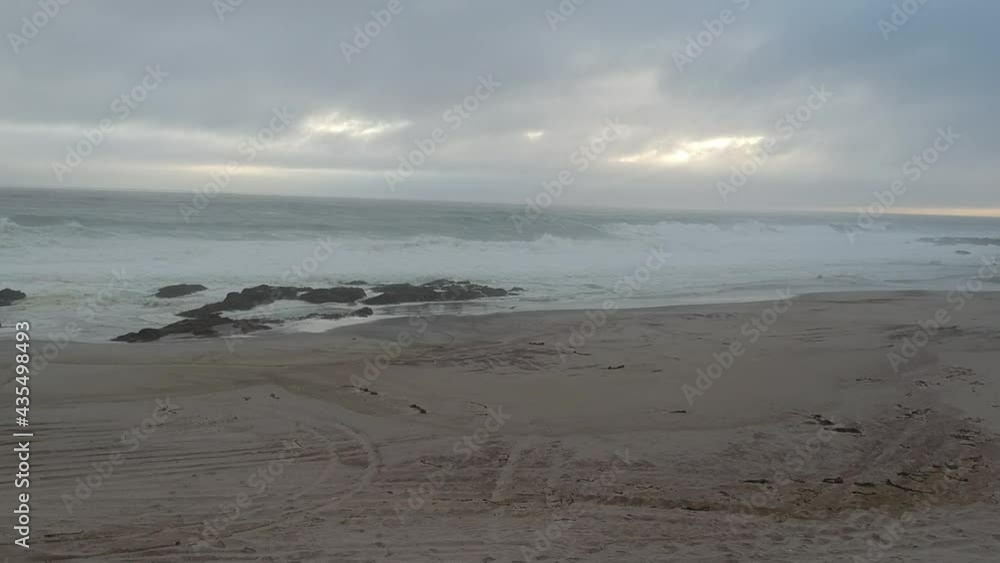 Mist and cloudy day at the beach waves below camera dark white clouds on the horizon rocks next to sandy beach camera are moving up and approaching the beach Aerial video. Mist and cloudy day at the beach waves below camera dark white clouds on the horizon rocks next to sandy beach camera are moving up and approaching the beach Aerial video.