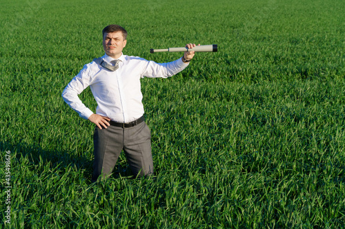 businessman poses with a spyglass, he looks into the distance and looks for something, green grass and blue sky as background