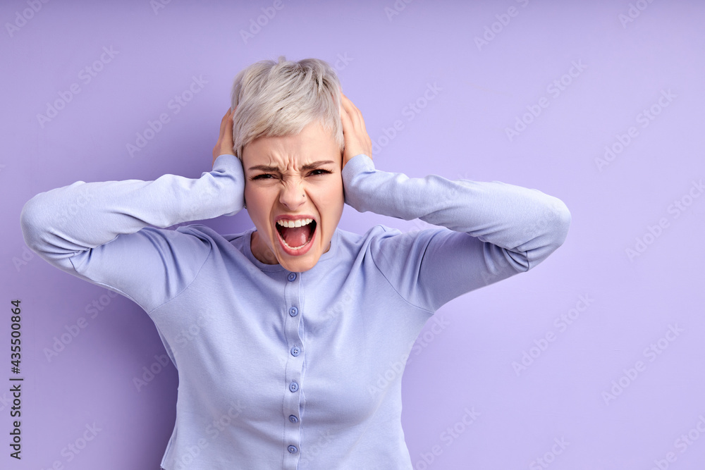 Inner pain. Devastated young caucasian woman closing ears with hands, screaming, on purple studio wall with empty space for your promotional content. Desperate female with short hair Inner pain. Devastated young caucasian woman closing ears with hands, screaming, on purple studio wall with empty space for your promotional content. Desperate female with short hair