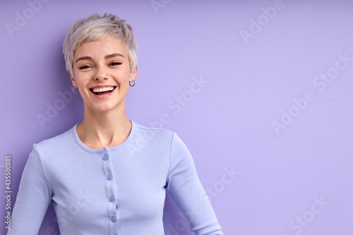 good-humored lady with short hair laughing, enjoying life, having fun, dressed casually, posing alone isolated on purple studio background. People lifestyle, human emotions concept