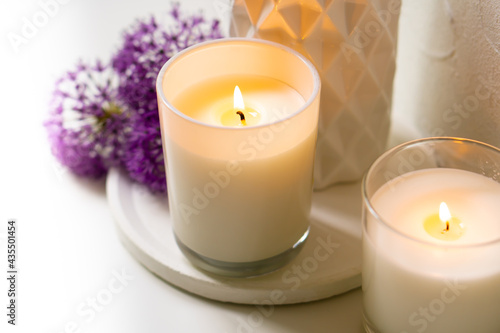 Burning candle and violet allium flowers on white tray