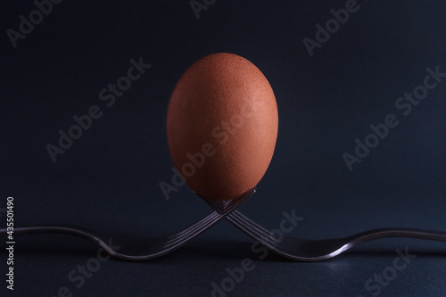 Egg on two forks. Chicken egg stands on two forks. Abstract still life, two forks and egg on a black background. 