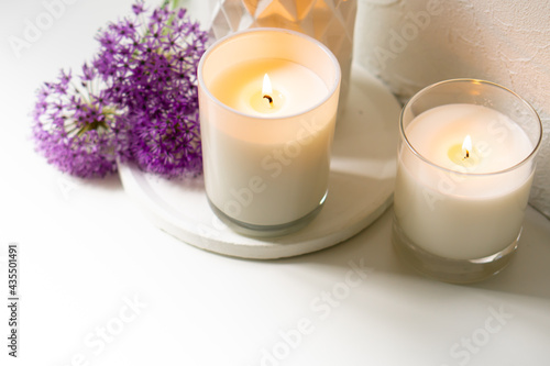 Burning candle and violet allium flowers on white tray
