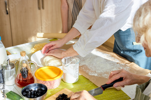 cropped family members roll out pizza dough together, preparing tasty pizza for dinner, cooking time. close-up photo of hands