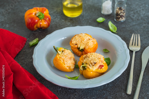 Stuffed yellow peppers with ricotta cheese and vegetables on a gray plate on a dark concrete background. Recipes for stuffed vegetables.