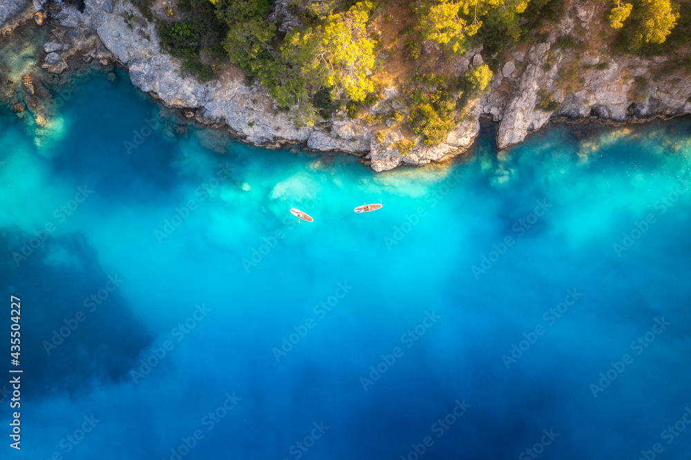 Aerial view of floating board and people on blue sea, rocks with trees at sunset in summer in Blue lagoon, Oludeniz, Turkey. Tropical landscape. Kayaks on clear water. Active travel. Top view of canoe