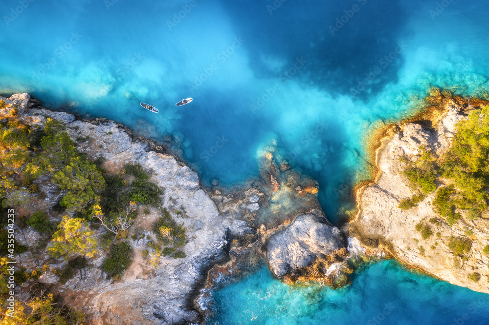 Aerial view of floating board and people on blue sea, rocks with trees at sunset in summer in Blue lagoon, Oludeniz, Turkey. Tropical landscape. Kayaks on clear water. Active travel. Top view of canoe