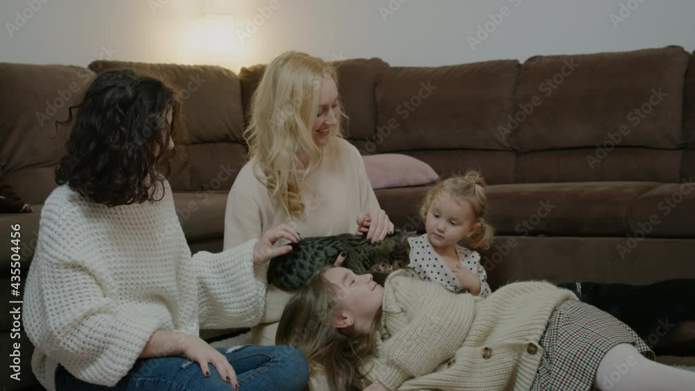Mother with daughters at home, stroking cat on floor by sofa Rbbro Young woman bonding with children Mother with daughters at home, stroking cat on floor by sofa Rbbro Young woman bonding with children