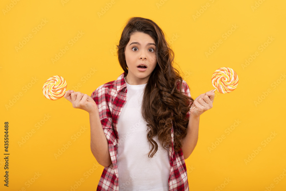 shocked teen girl with curly hair hold lollipop caramel candy on yellow background, confectionery. shocked teen girl with curly hair hold lollipop caramel candy on yellow background, confectionery.