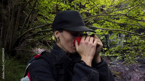 Wallpaper Mural young woman in cap enjoying a drink in a red mug and watching a beautiful waterfall in the forest during a break on her route through the mountains. activities in the mountains. weekend getaway Torontodigital.ca