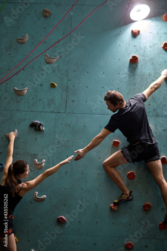 Confident woman and man mountaineers climbing artificial rock wall with belay at bouldering gym, in sportswear, rear view on professional sport people workout training, supporting each other