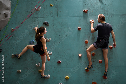Athlete sporty woman and man in sportive outfit practicing rock climbing on artificial rock in sport club. Extreme sports and bouldering concept.