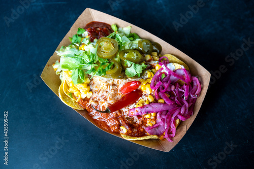 Chilli con carne in street food takeaway box with pickled onions, jalapeños, parsley, corn and hot sauce.
