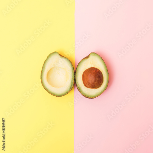 Two upsidedown  halves of avocado on a pastel yellow and pink background.