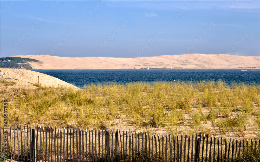 Dune and a barrier protecting the dunes at Cap-Ferret with the Dune of Pilat in the background. Commune in the Gironde department in southwestern France