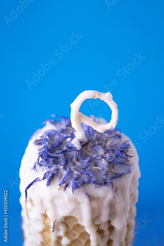 Vertical photo of candle made of beeswax and soy wax with dried cornflowers on a blue background. Photo was shot in macro style for your cozy design.