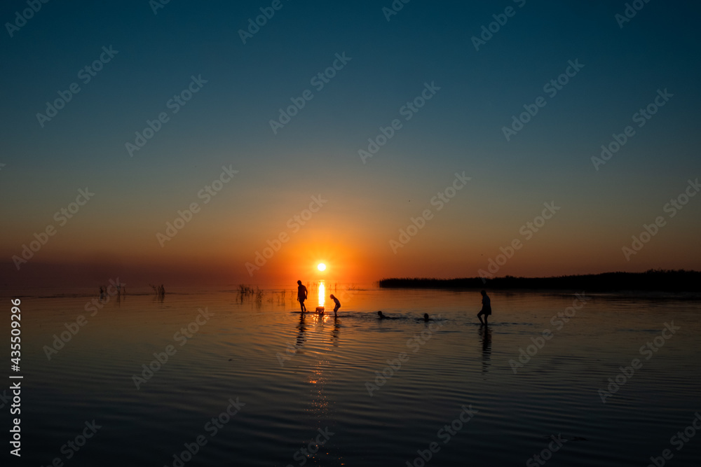 Silhouette of a big family walking on the lake at sunset. Concept of traveling family and enjoying the outdoors and the nature.