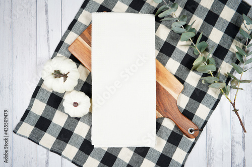 Kitchen tea towel dish cloth mockup. On-trend farmhouse aesthetic flatlay svg craft product mock up with black plaid table cloth and white pumpkins on a white wood background. Negative copy space. photo