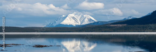 Panoramic shot of snow capped mountain view scenery seen in northern British Columbia during spring time with blue sky day and clouds. Magnificent vista and relaxing scene. 