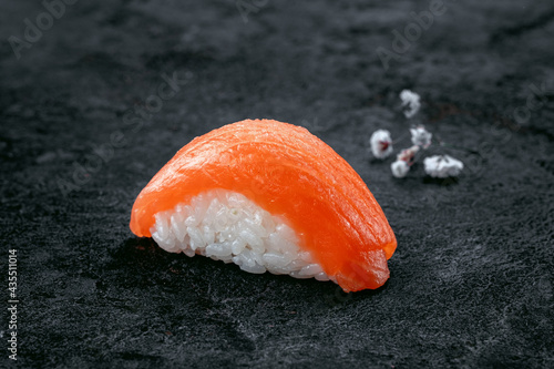 One nigiri sushi with salmon on a stone dark background with a sprig of sakura. Japanese dish sushi of fresh fish