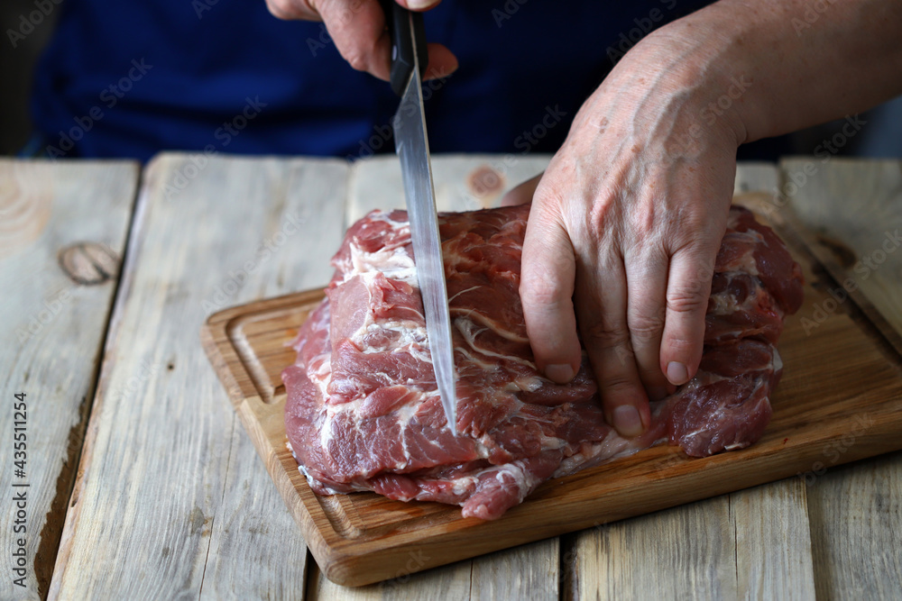 Male hands with a knife cut raw meat on the board. The cook is cutting raw meat.