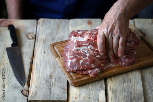 Male hands with a knife cut raw meat on the board. The cook is cutting raw meat.