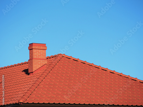 Εκτύπωση καμβά Red roof tiles with red brick chimney on blue sky background.