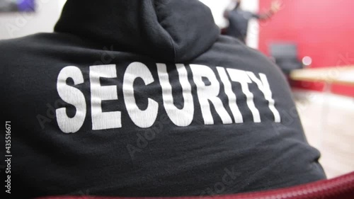 A rearview of security personnel sitting on a chair with text on his uniform in HD photo