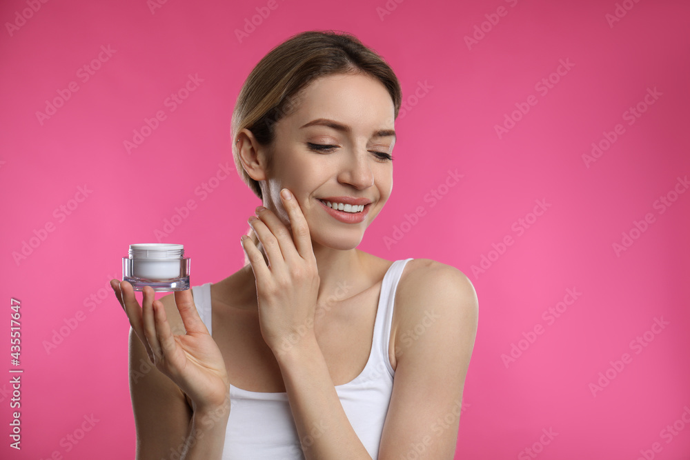 Young woman applying facial cream on pink background Young woman applying facial cream on pink background