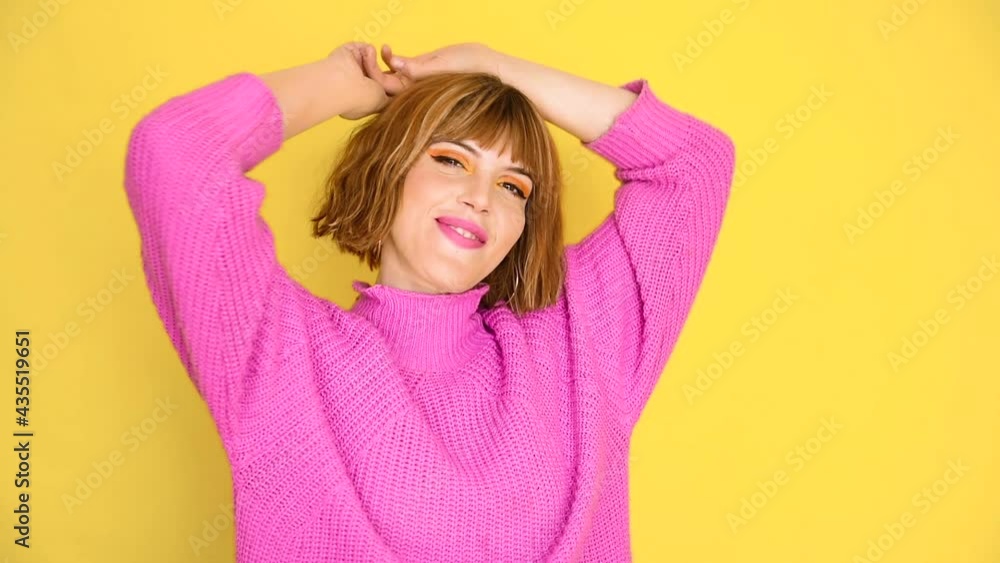 A girl stands in front of a yellow background with short hair and a pink sweater she is dancing, smiling, calmly and serene. Alone fun. Emotions. A girl stands in front of a yellow background with short hair and a pink sweater she is dancing, smiling, calmly and serene. Alone fun. Emotions.