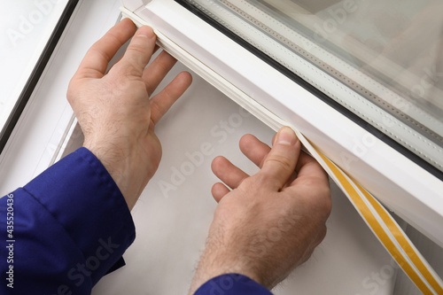 Worker putting rubber draught strip onto window indoors, closeup photo