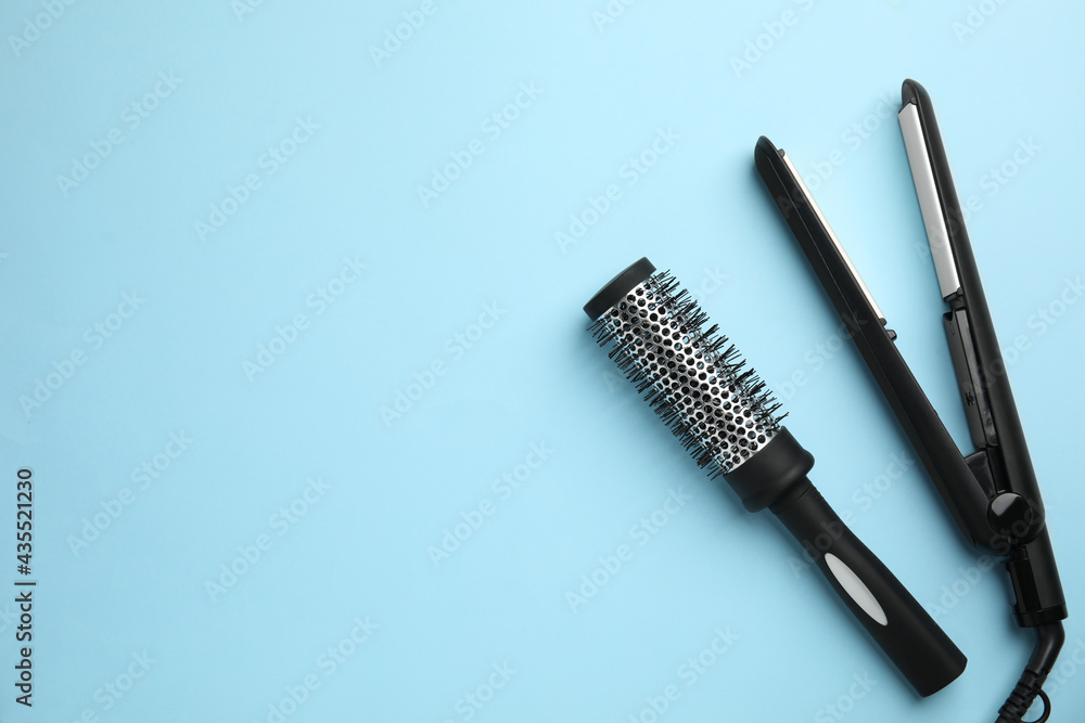 Hair straightener and round brush on light blue background, flat lay. Space for text Hair straightener and round brush on light blue background, flat lay. Space for text