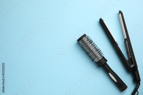 Hair straightener and round brush on light blue background  flat lay. Space for text