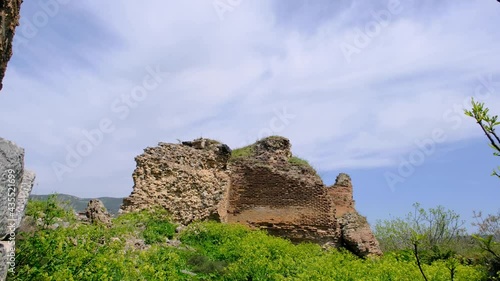 Old ancient and ruins city walls remanings in iznik with abandoned and brownfield city walls made of stone and red bricks with yellow and purple color flowers around the green grass. photo