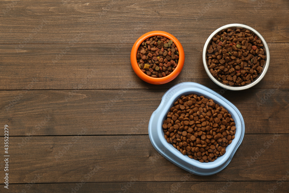 Dry food in pet bowls on wooden background, flat lay. Space for text Dry food in pet bowls on wooden background, flat lay. Space for text
