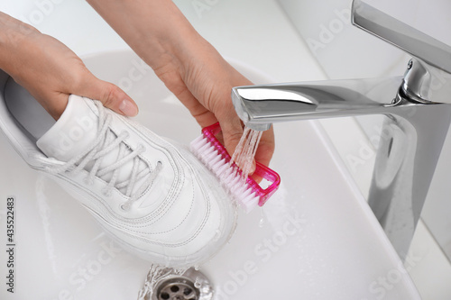 Woman washing shoe with brush under tap water in sink, closeup photo