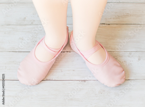 Little girl ballerinas feet in pink ballet shoes standing on a wooden surface , dancing concept, ballet