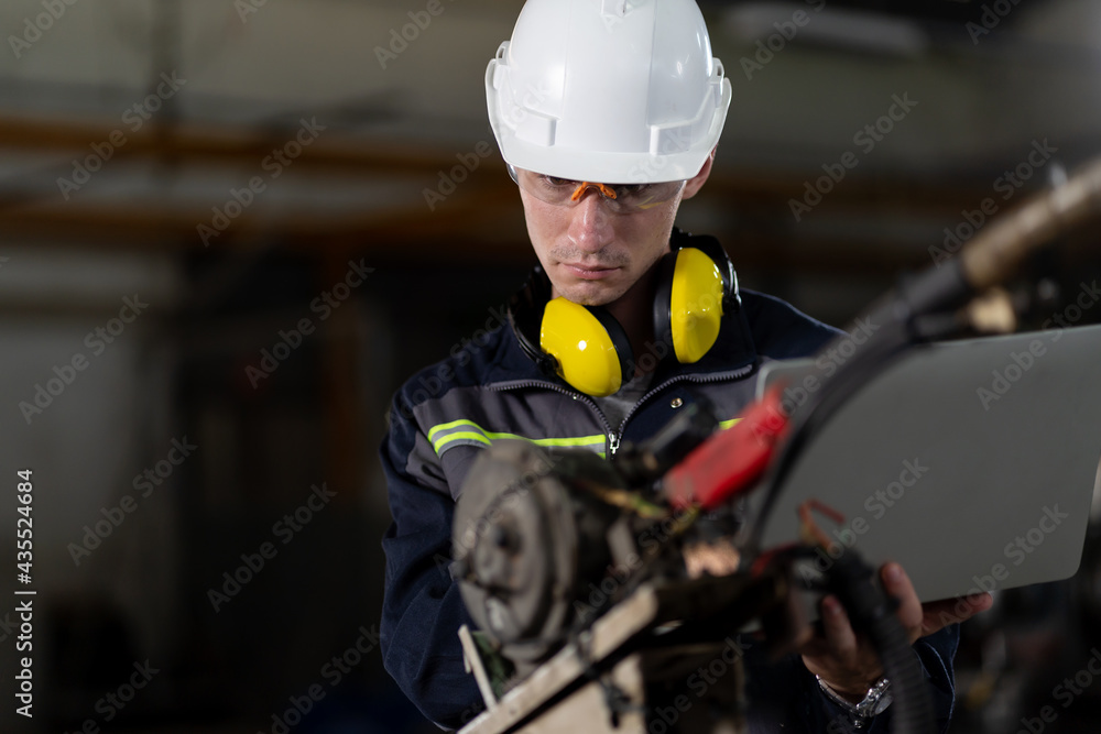Fototapeta premium Male engineer worker working with computer notebook for control automatic robotic arm machine in the factory. Male technician worker maintenance automatic robotic hand in smart factory