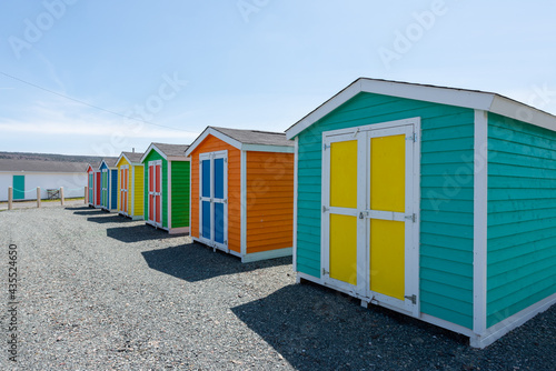 Multiple wooden sheds with colorful double doors. The buildings are blue, yellow and green storage buildings. The colorful huts have white trim on the edges. The background is a blue sky with clouds.  © Dolores  Harvey