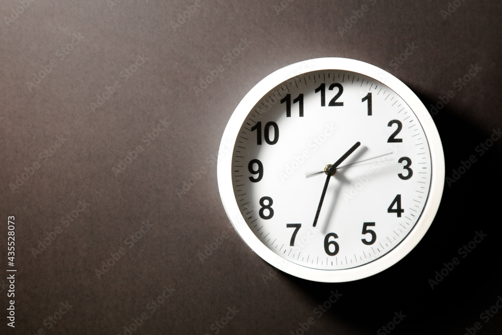Close-up of a modern fashioned white Wall Clock with numerals on the clock face. Clock with white frame on a black background. Pointers showing the time. front view of the Watch out of center Close-up of a modern fashioned white Wall Clock with numerals on the clock face. Clock with white frame on a black background. Pointers showing the time. front view of the Watch out of center