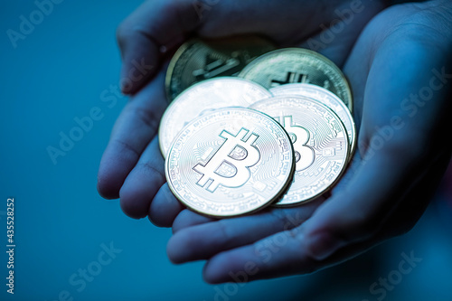 Fototapeta Naklejka Na Ścianę i Meble -  Shiny bitcoins in hand palm over dark blue background. Cryptocurrency market crash concept.