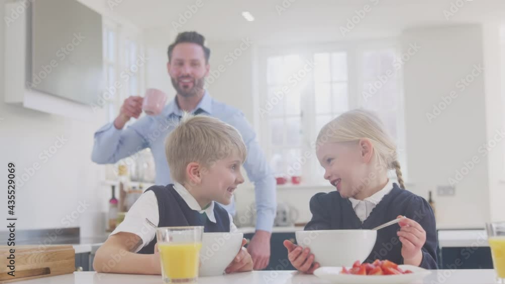 Two children wearing school uniform in kitchen eating breakfast as businessman father gets ready for work - shot in slow motion Two children wearing school uniform in kitchen eating breakfast as businessman father gets ready for work - shot in slow motion