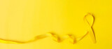 Yellow Ribbon on yellow background for supporting people living and illness. July Sarcoma cancer, Suicide prevention day, Childhood Cancer Awareness month concept