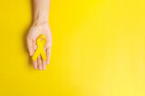 hand holding Yellow Ribbon on yellow background for supporting people living and illness. Suicide prevention day, Sarcoma cancer and Childhood Cancer Awareness month concept