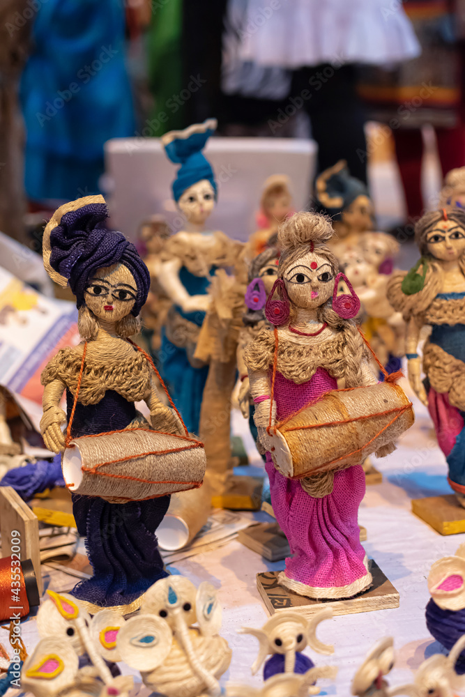 Handmade puppet models of musicians and dancers with traditional costumes made of Jute isolated on blurred background is displayed in a street shop for sale. Indian handicraft and art