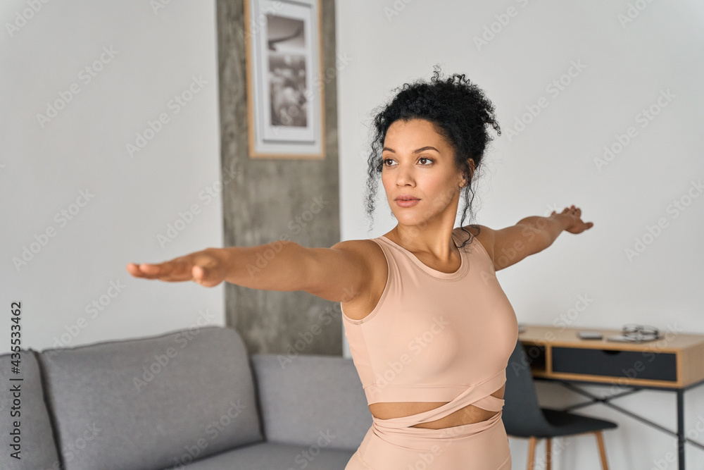 Young healthy African American mixed race girl standing at home doing fitness exercises meditating breathing deeply feeling balance, harmony and no stress. Mental health care concept.